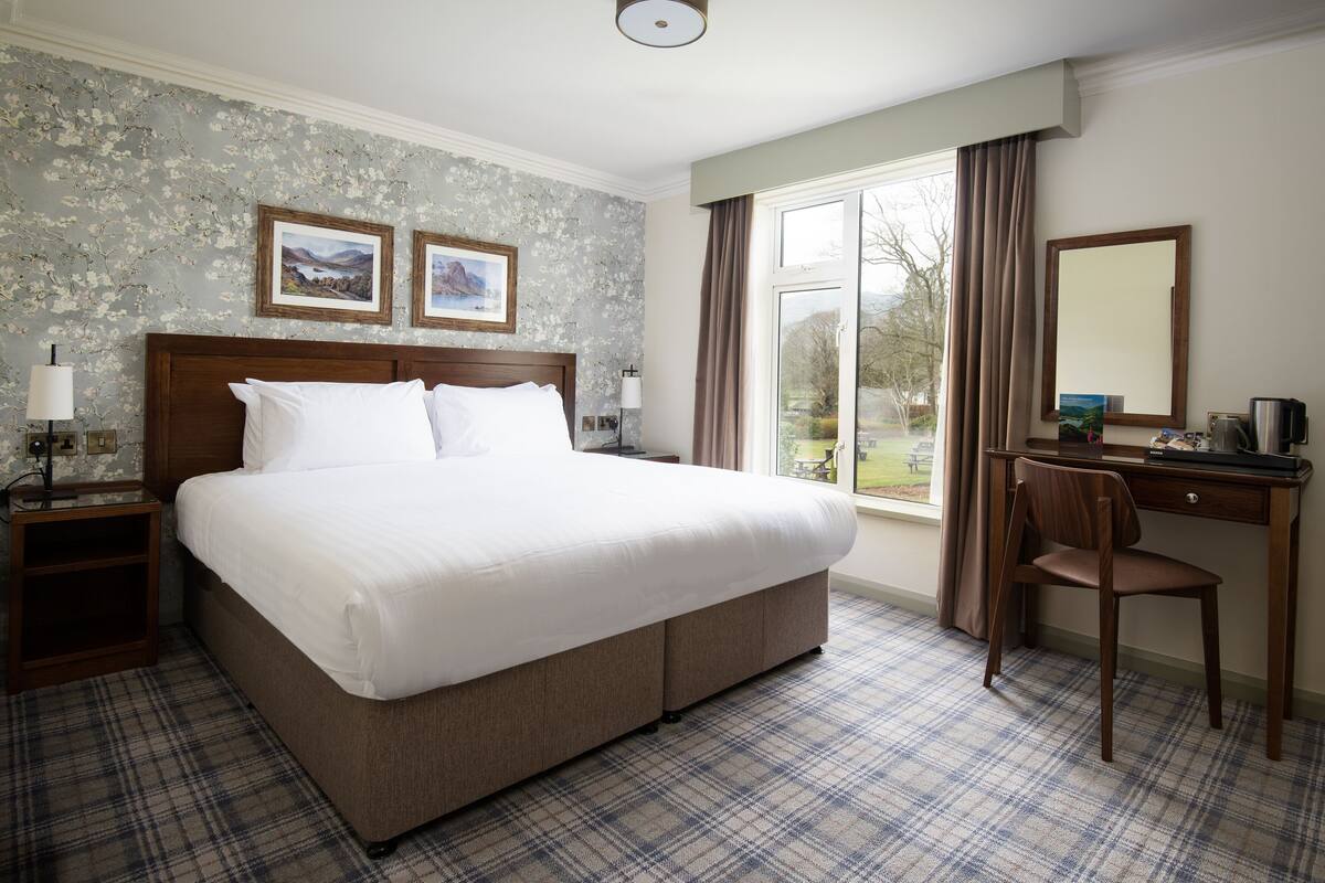 A hotel room with a large bed, a desk with a chair, and two framed pictures on the wall.