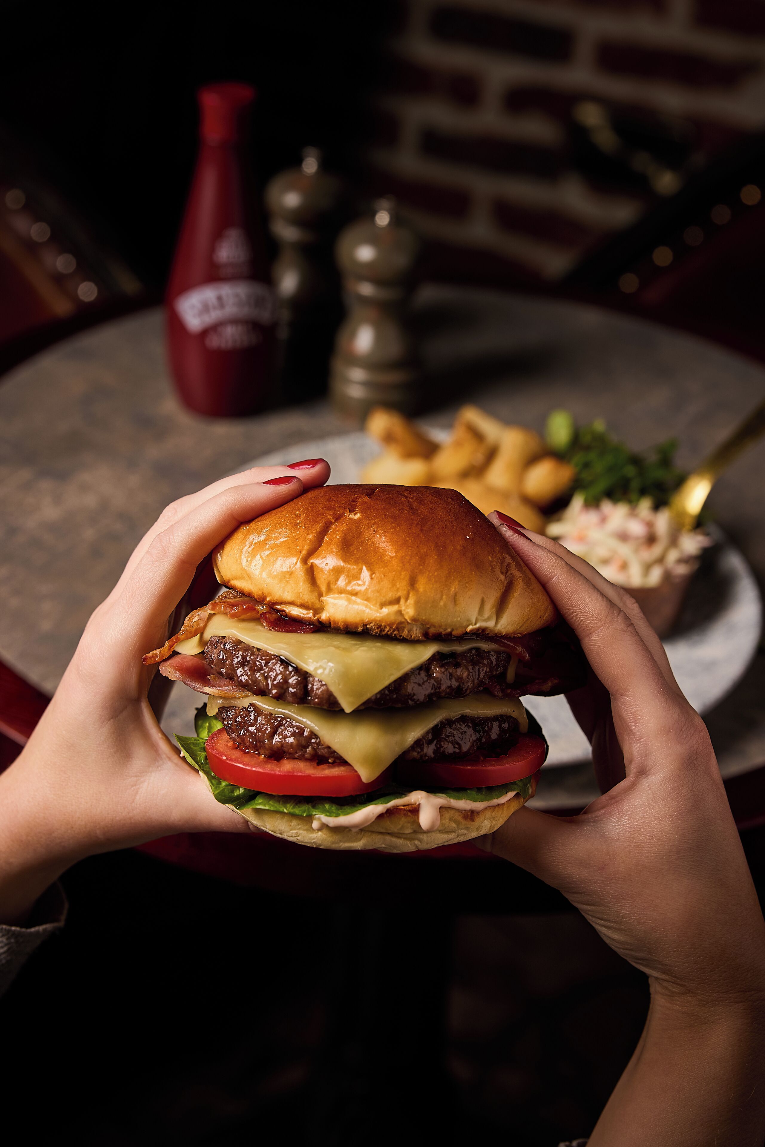 A close-up of a person holding a burger with a bun, cheese, lettuce, tomato, and a patty.