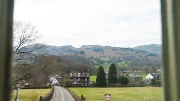 A rural road with stone walls and houses, a no entry sign, and a view of hills in the distance.