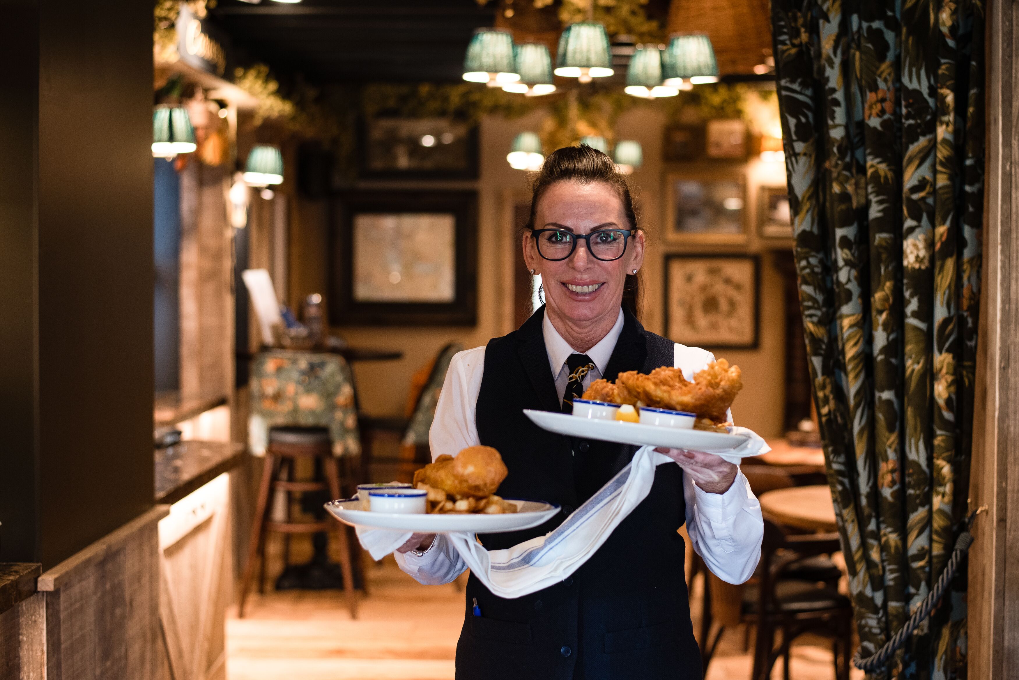 Una persona sosteniendo platos de comida frita en un restaurante con decoración de madera y luces colgantes.