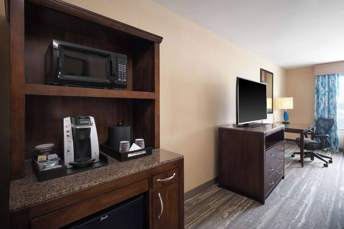 A hotel room with a kitchenette, including a microwave, coffee maker, and a flat-screen TV on a wooden cabinet.