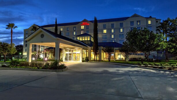 A hotel with a well-lit entrance, a covered area, and a large building in the background. - Hilton Garden Inn Houston/Bush Intercontinental Airport (Houston)