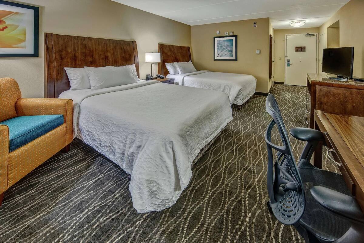 Une chambre d’hôtel avec deux lits, un bureau avec une télévision, une chaise et un tapis de course.