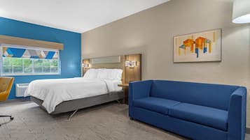 A hotel room with a bed, a blue sofa, a chair, and a painting on the wall.