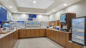 A modern breakfast area with wooden cabinets, a yogurt dispenser, and a coffee machine. - Holiday Inn Express Hotel & Suites Charlotte by IHG (Charlotte)