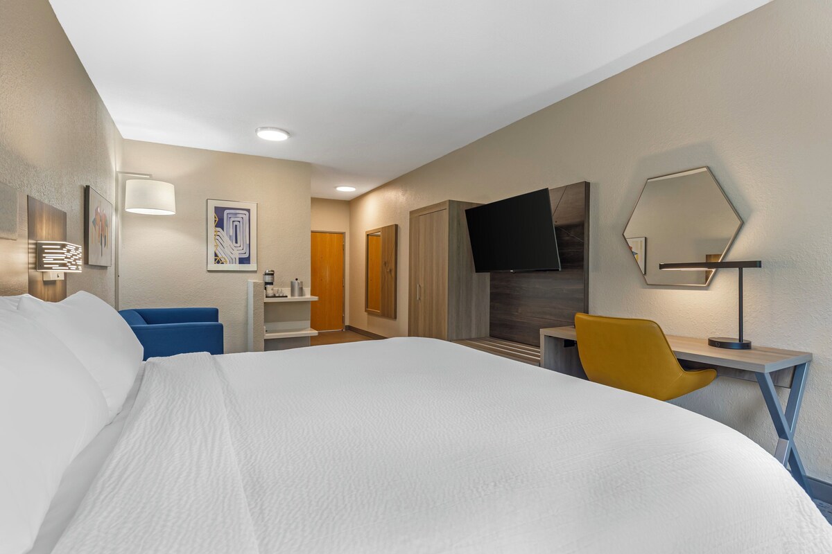 Une chambre d’hôtel avec un grand lit, un bureau avec une chaise, une télévision et des œuvres d’art accrochées aux murs.