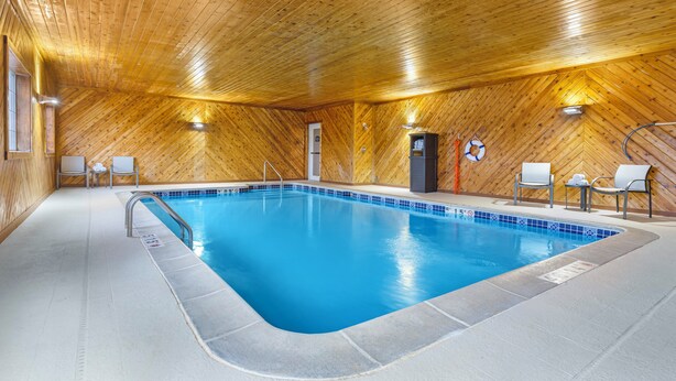 Une piscine intérieure avec des murs et un plafond en bois, un sol carrelé et quelques chaises disposées autour de la piscine.