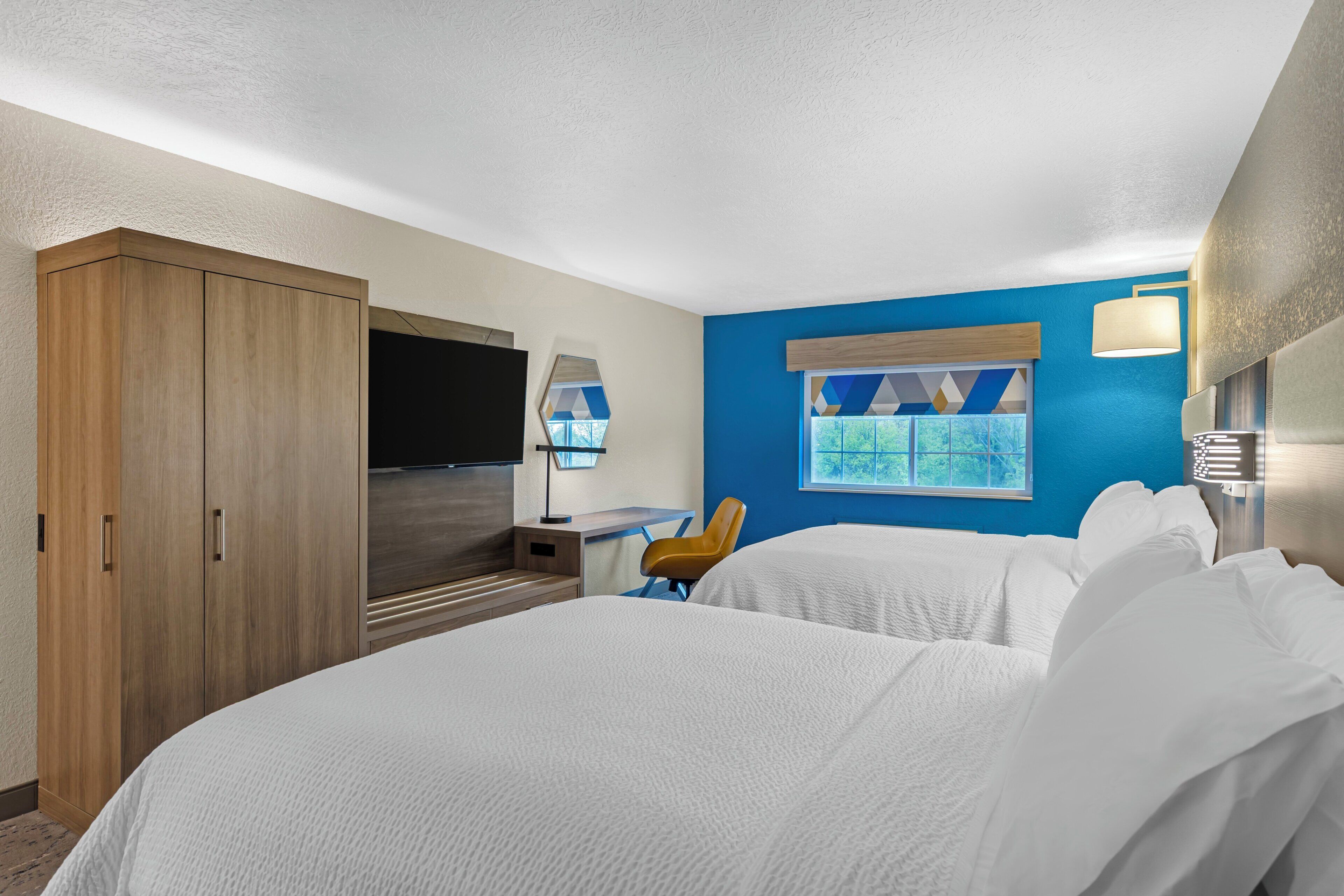 Ett hotellrum med en säng, ett skrivbord, en stol, en tv och en garderob.