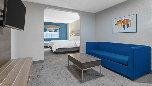 A modern hotel room with a blue sofa, a wooden coffee table, a flat-screen TV, and a painting on the wall. - Holiday Inn Express Hotel & Suites Charlotte by IHG (Charlotte)