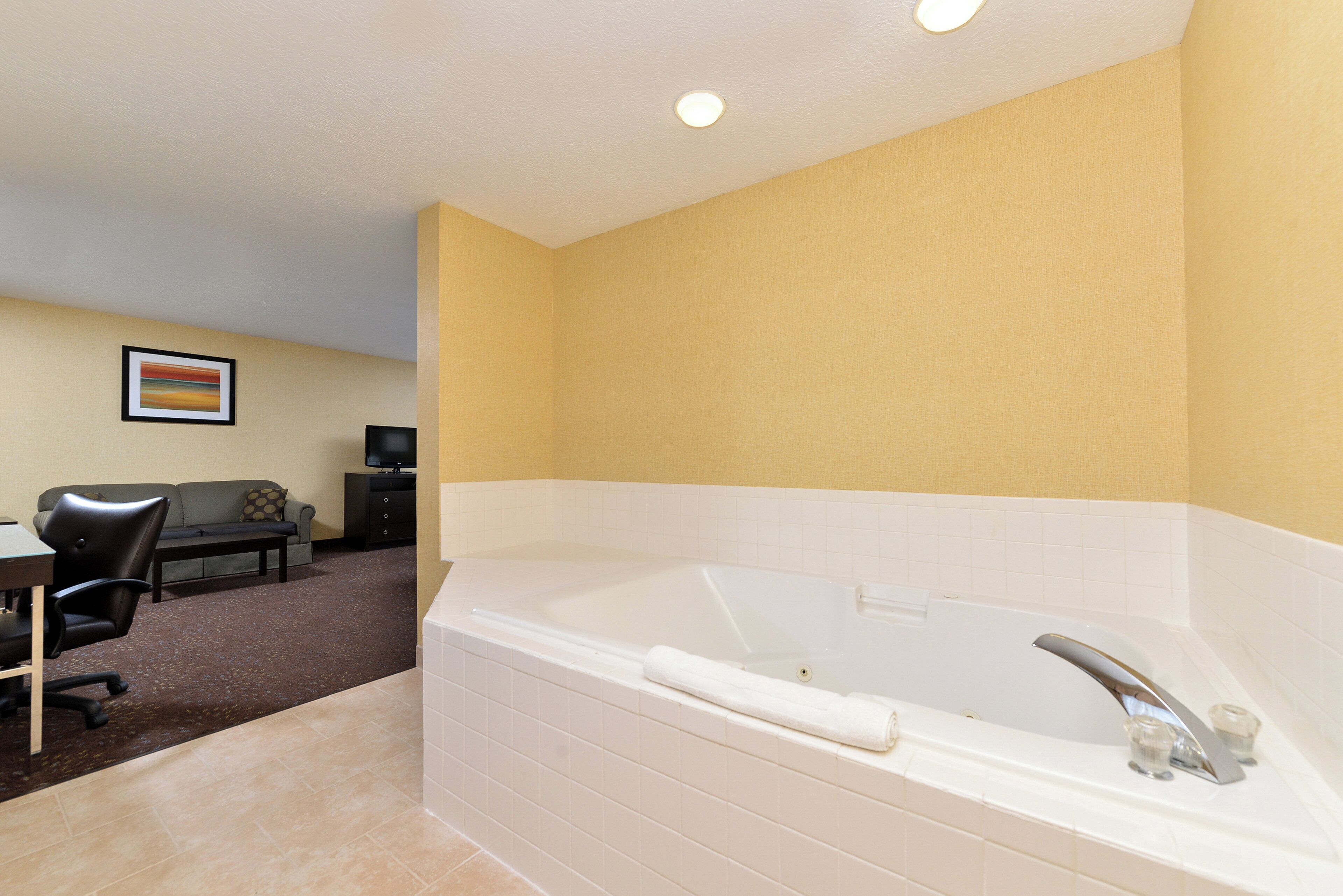 A hotel room with a large bathtub, a dining area with a table and chairs, and a television.