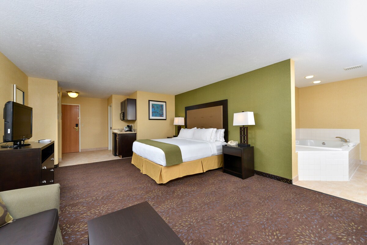 Une chambre d’hôtel comprenant un lit, des tables de chevet, un bureau avec une télévision, une salle de bain avec une baignoire et un sol recouvert de moquette.