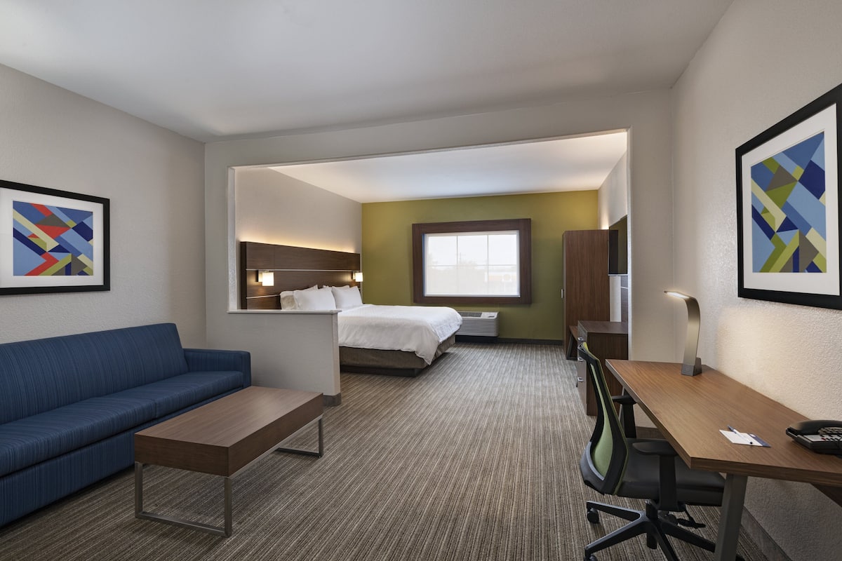 A hotel room with a blue sofa, a wooden desk, a bed, and a window.