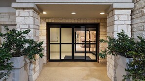 A building entrance with a stone facade, a glass door, and potted plants on either side. - Holiday Inn Express Hotel & Suites Cedar Park by IHG (Cedar Park)