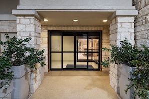 A building entrance with a stone facade, a glass door, and potted plants on either side. - Holiday Inn Express Hotel & Suites Cedar Park by IHG (Cedar Park)