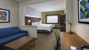 Quarto de hotel com cama, escrivaninha, cadeira, sofá e janela.