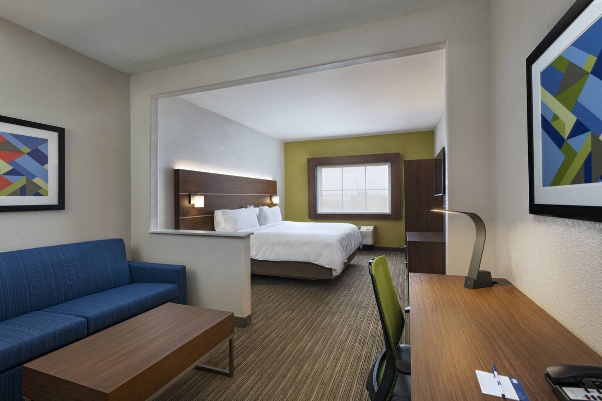 A hotel room with a bed, a desk, a chair, a sofa, and a window.