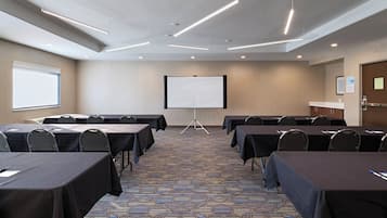 Un salón de conferencias con mesas, sillas, una pantalla de proyector y piso alfombrado.