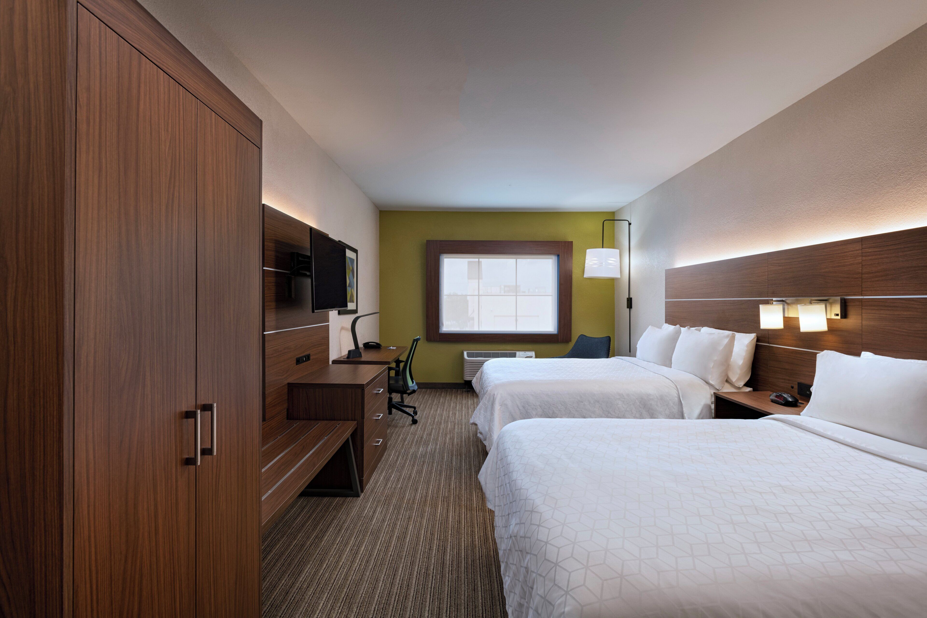 A hotel room with two beds, a desk, a chair, a TV, and a window.