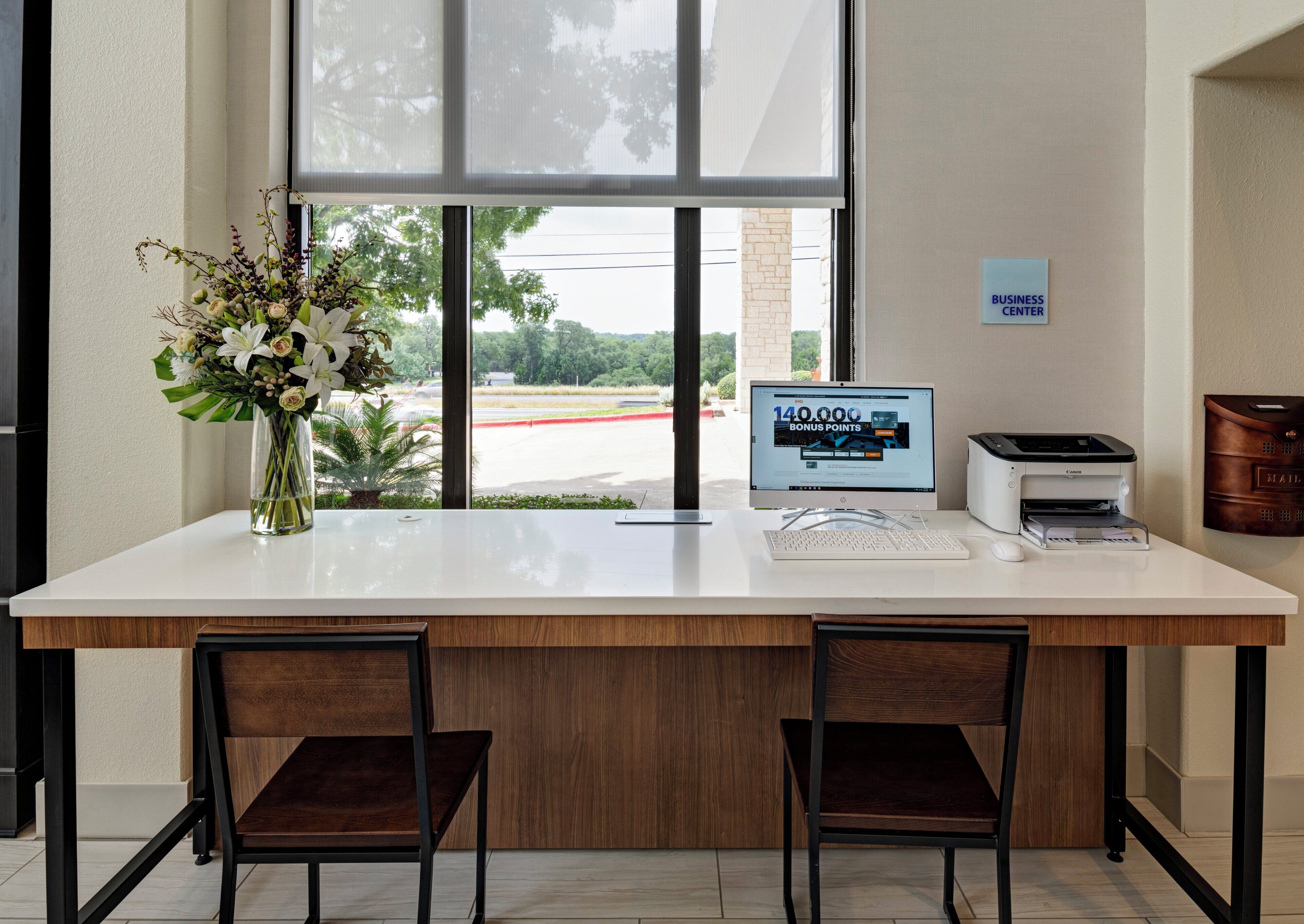 A reception desk with a computer, printer, and a vase of flowers.