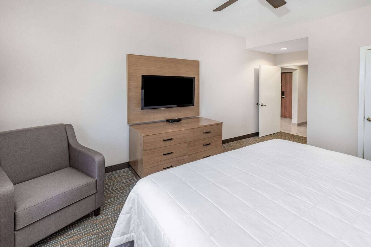 Une chambre d’hôtel comprenant un lit, un canapé, un téléviseur fixé sur un panneau en bois et une porte donnant sur une autre pièce.