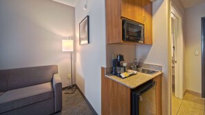 Habitación de hotel compacta con kitchenette, un sofá y una lámpara.