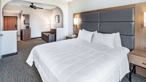 Habitación de hotel con una cama grande, un escritorio, una silla, una lámpara de escritorio, un teléfono y un ventilador de techo.