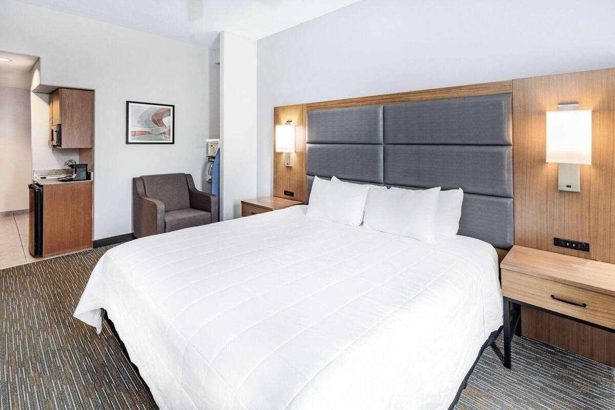 Une chambre d’hôtel avec un grand lit, un bureau, une chaise, une petite kitchenette et une lampe fixée au mur.