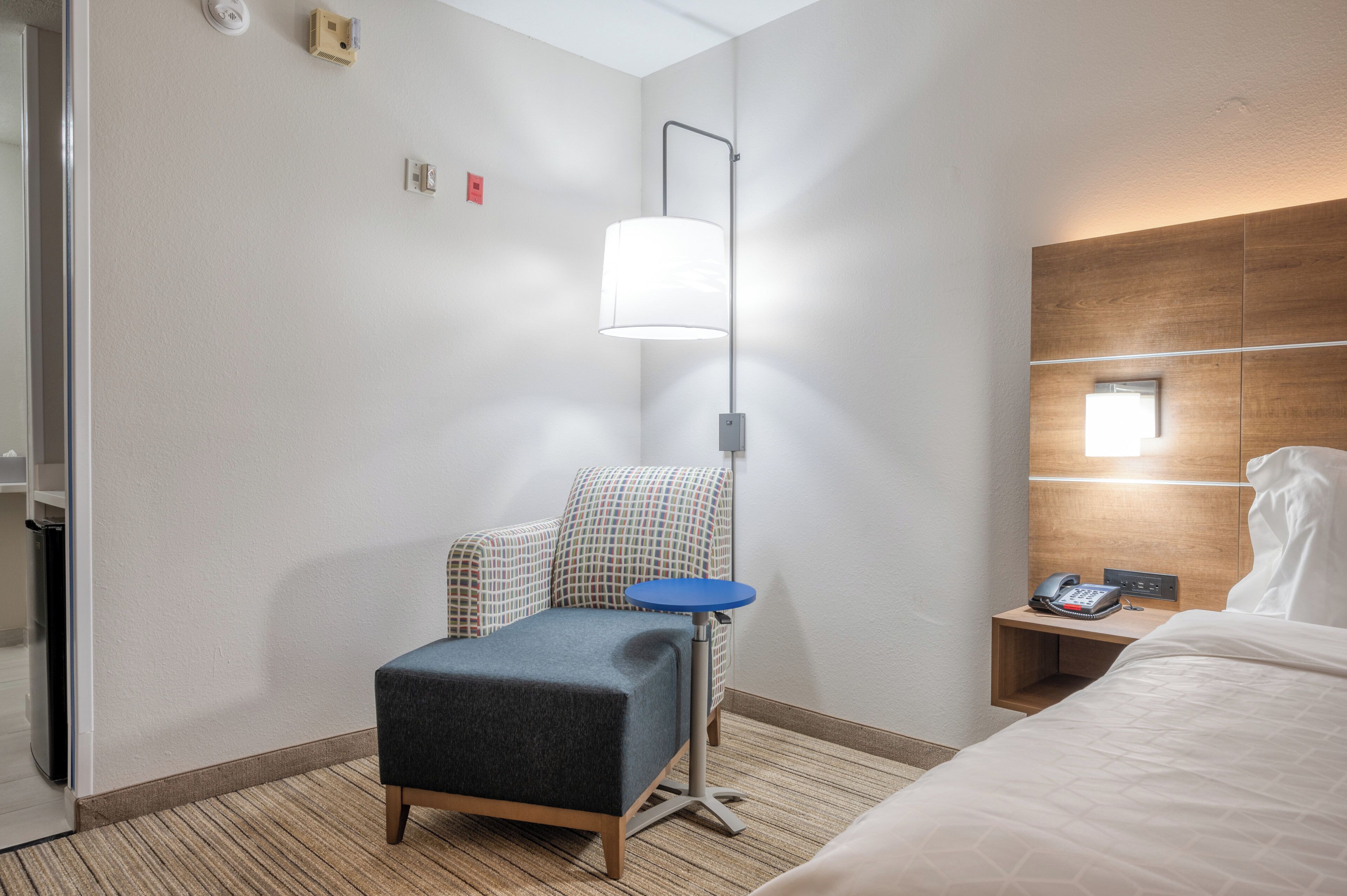 Habitación de hotel con cama, escritorio con teléfono, silla, lámpara de pie y una mesita.