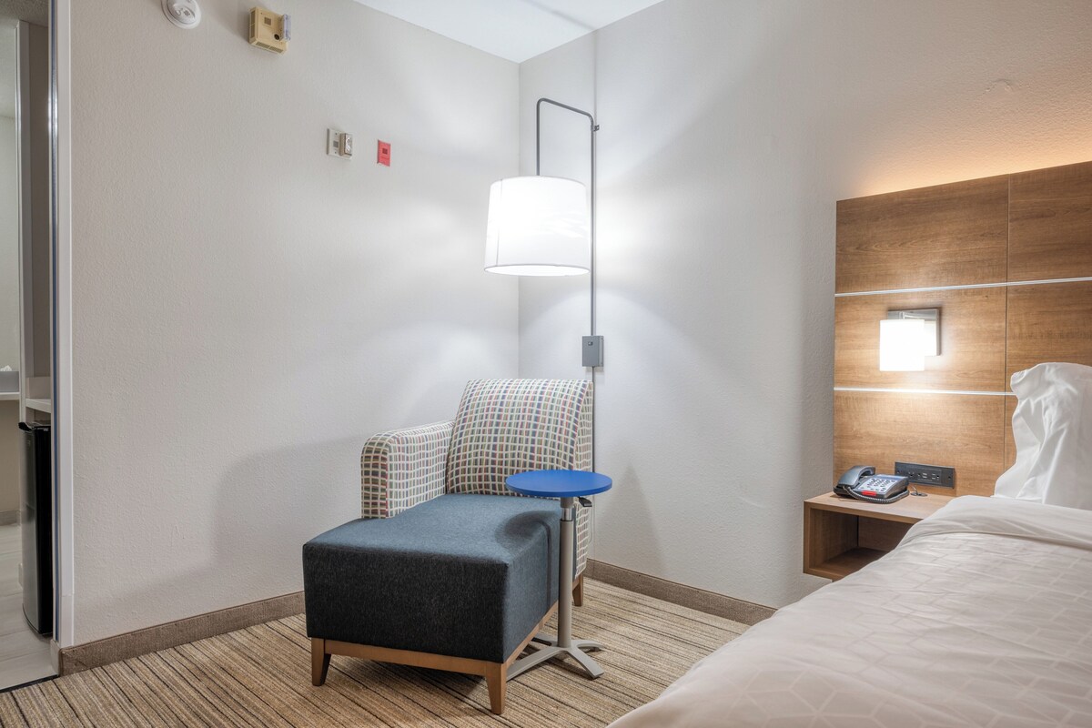Ein Hotelzimmer mit Bett, einem kleinen Tisch, einem Sessel, einer Lampe und einem Nachttisch mit Telefon.