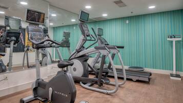 Un gimnasio con diferentes máquinas de cardio, un espejo grande y paredes verde azulado a rayas.