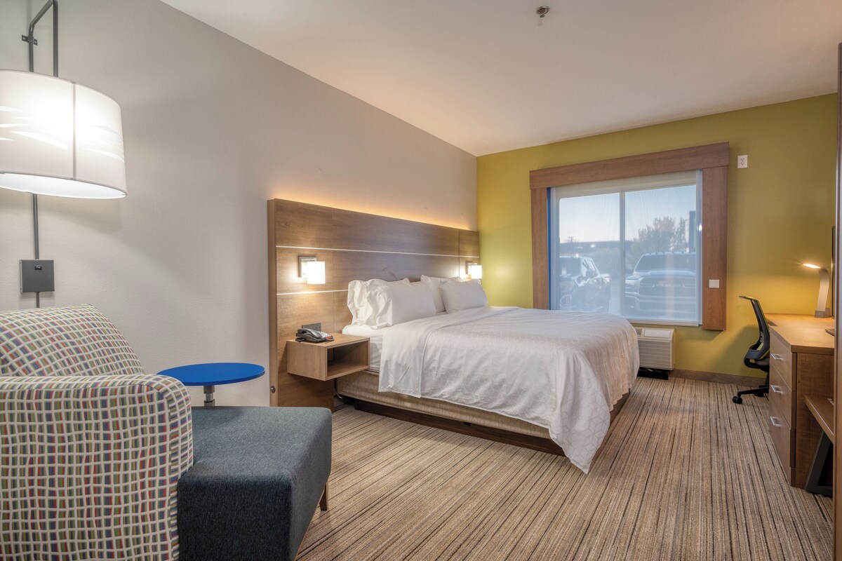 Ein Hotelzimmer mit Bett, Nachttisch, Lampe, Stuhl, Schreibtisch und Fenster.