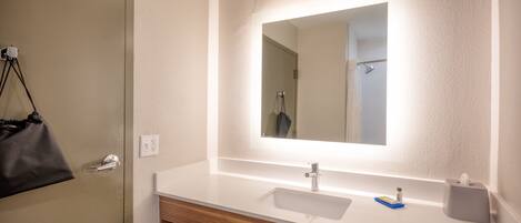 Un baño con lavamanos blanco, un espejo con luz, un perchero para toallas y un mueble de tocador de madera.