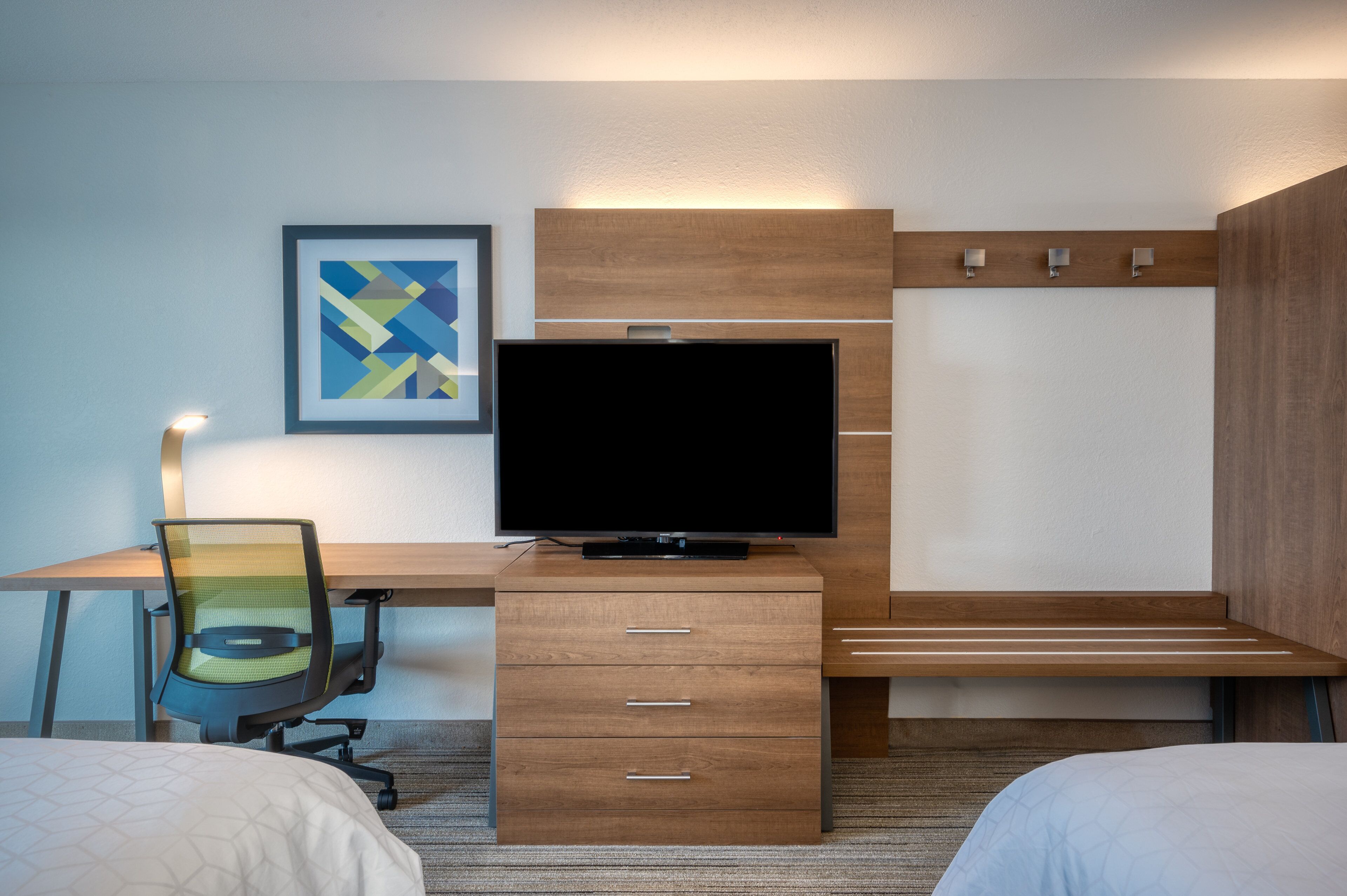 A hotel room with a wooden desk, a television, a chair, and a bed.
