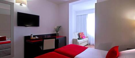 A hotel room with two beds, a TV, a desk, and a window with curtains.
