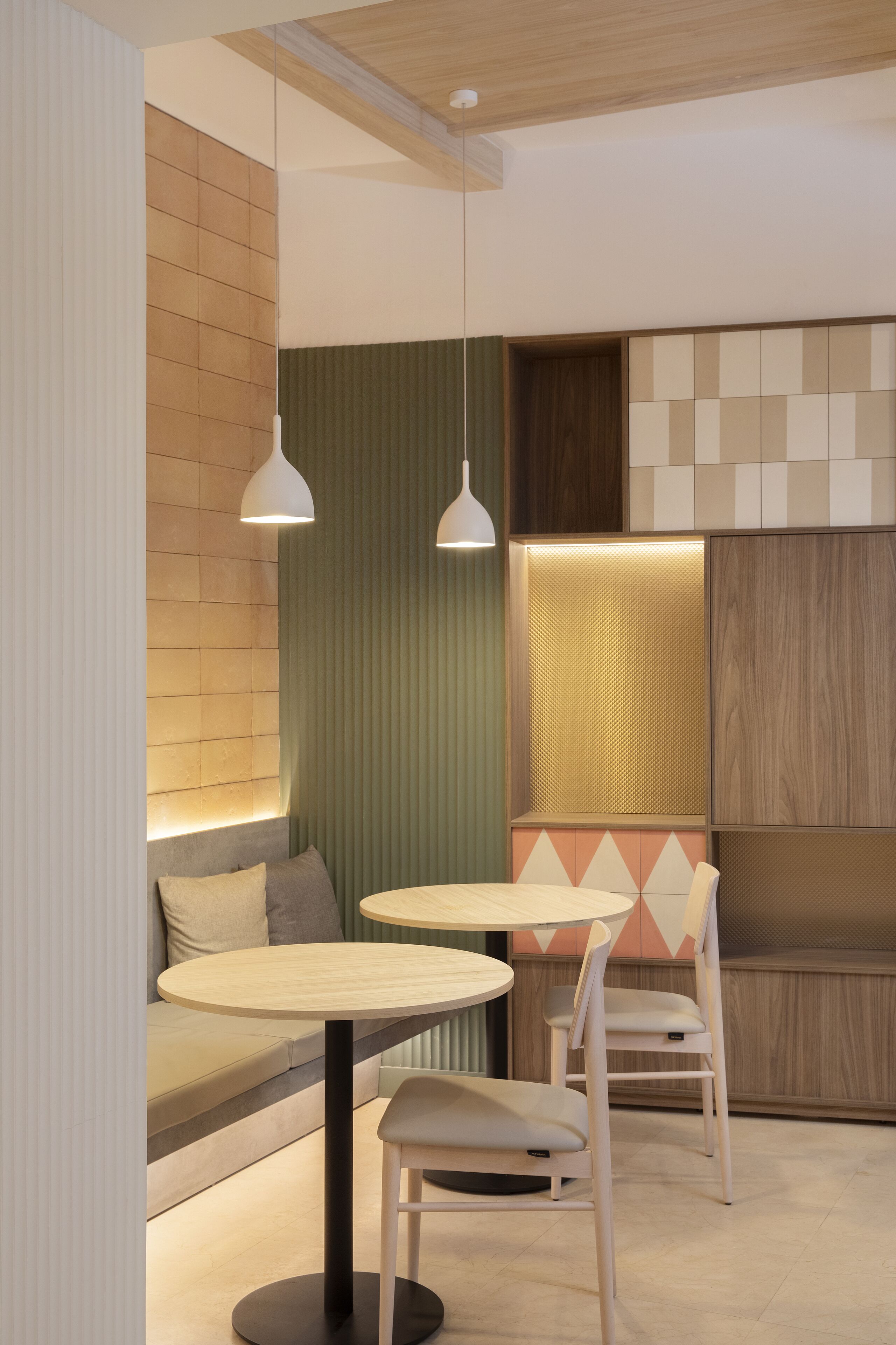 Un interior moderno con una mesa redonda y dos sillas, un banco acolchado y una pared con motivos geométricos.