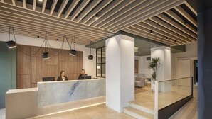 A modern reception area with a marble counter, wooden paneling, and pendant lighting. - Grupotel Gravina (Barcelona)