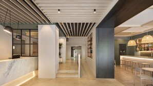 A modern hotel lobby with a marble reception desk, a staircase, and a bar area with stools. - Grupotel Gravina (Barcelona)