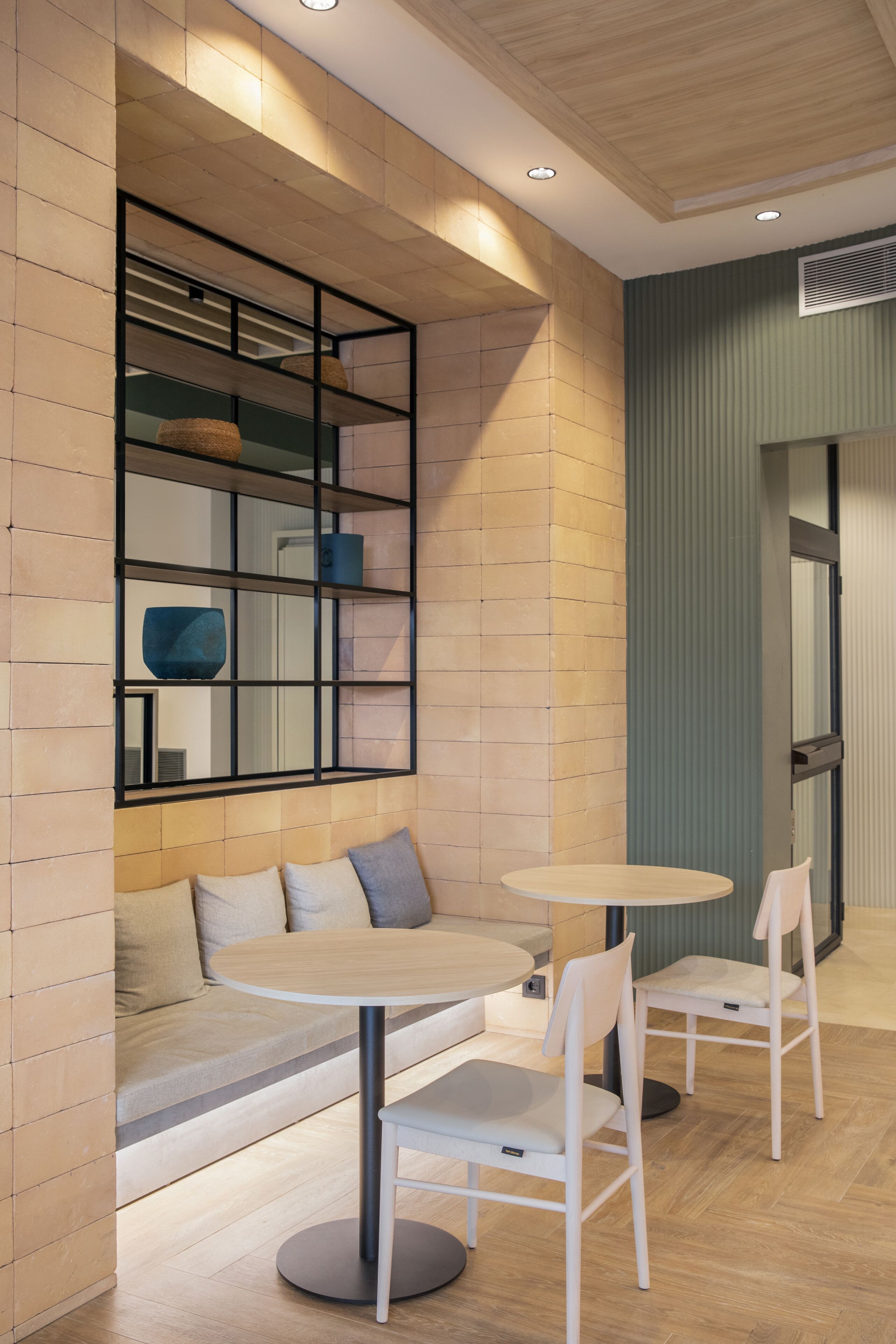 Um interior moderno com uma mesa redonda e duas cadeiras, um banco acolchoado e uma prateleira suspensa com objetos decorativos.