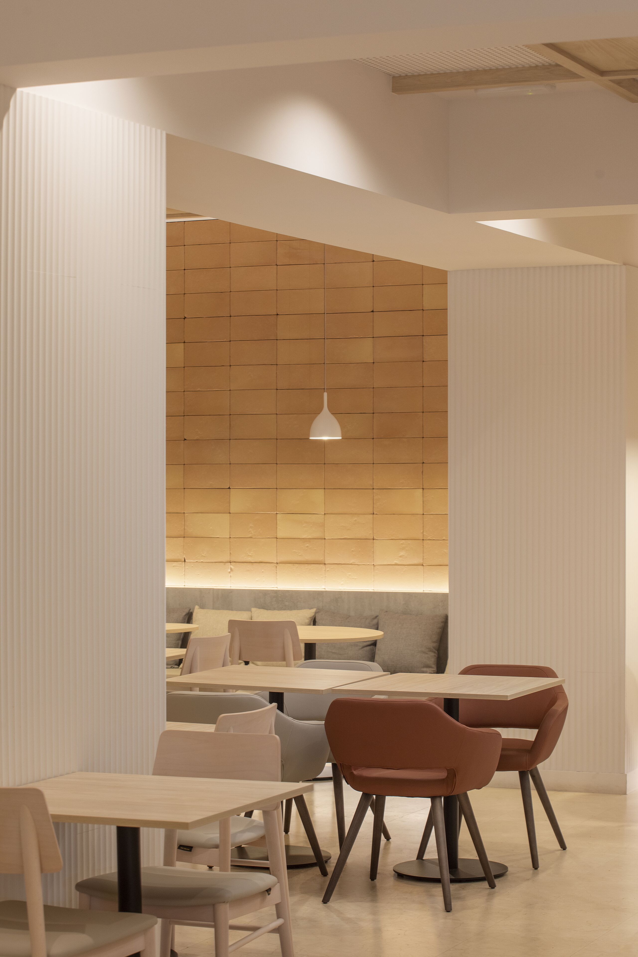 A modern dining area with a wooden wall, a hanging light fixture, and a seating arrangement.