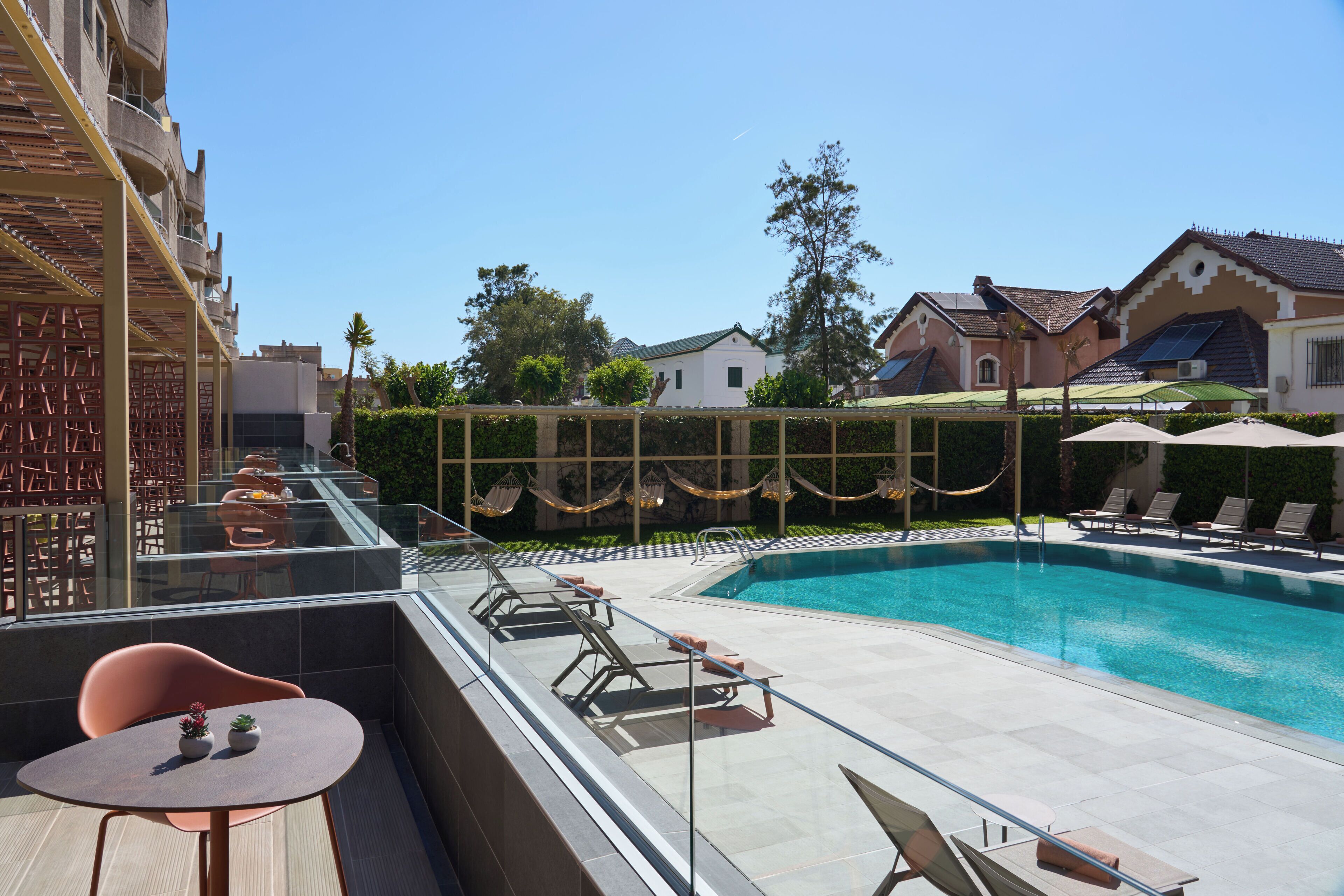 A rooftop pool area with lounge chairs and a table, surrounded by a glass balustrade.