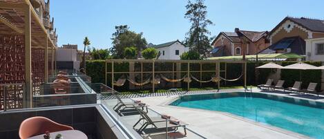 A rooftop pool area with lounge chairs and a table, surrounded by a glass balustrade.