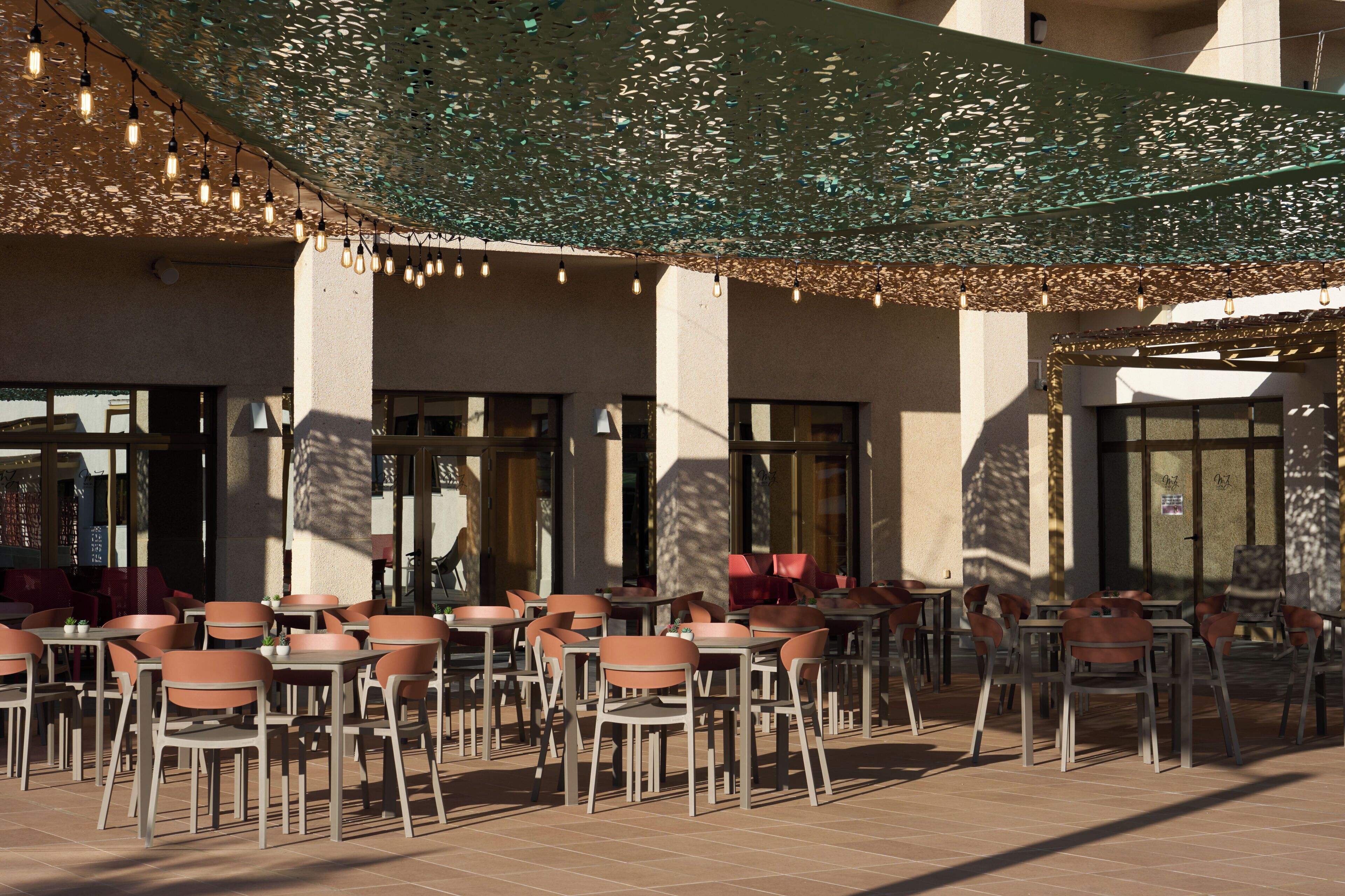 An outdoor seating area with tables and chairs, a decorative ceiling, and large windows.