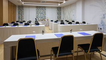 Un salón de conferencias con varias mesas, sillas y un fondo de papel tapiz con motivos florales.