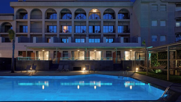 Un hotel con piscina, varios balcones e iluminación exterior.