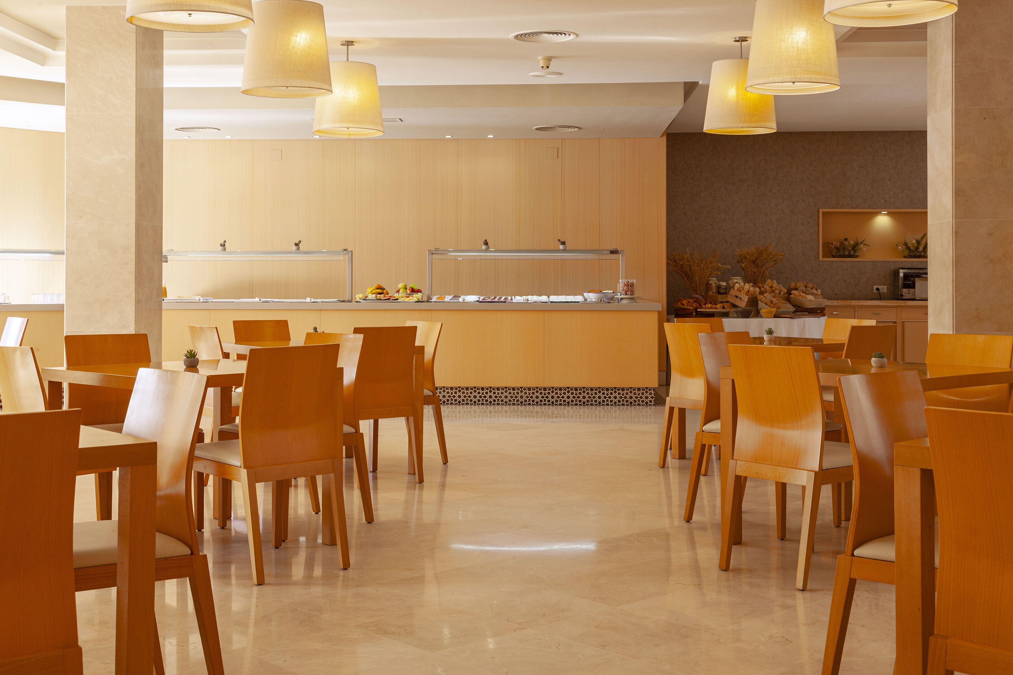 Un comedor moderno con sillas y mesas de madera, un mostrador de buffet e iluminación colgante.