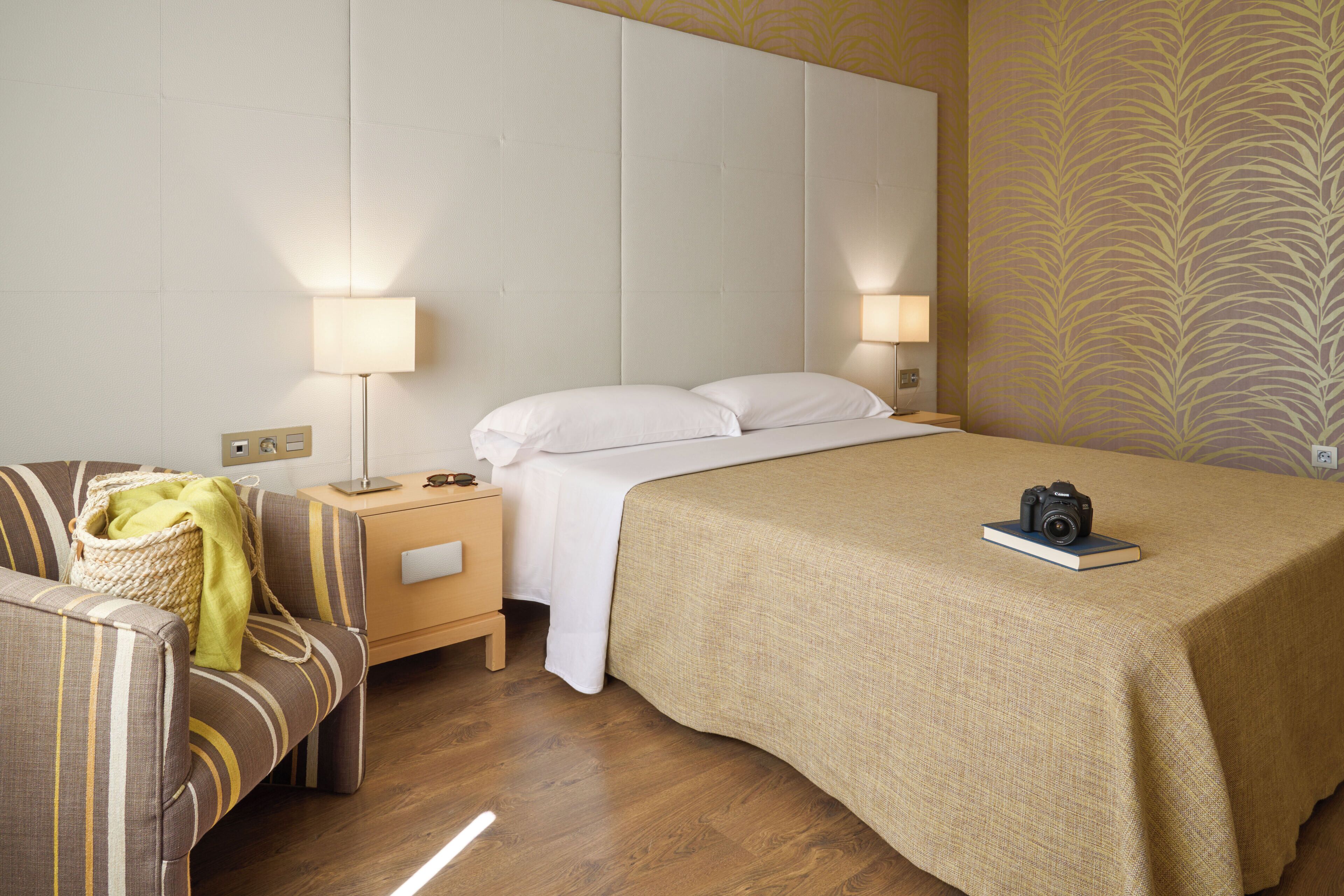 Una habitación de hotel con una cama, una mesita de noche, una lámpara, una silla y una cámara sobre la cama.