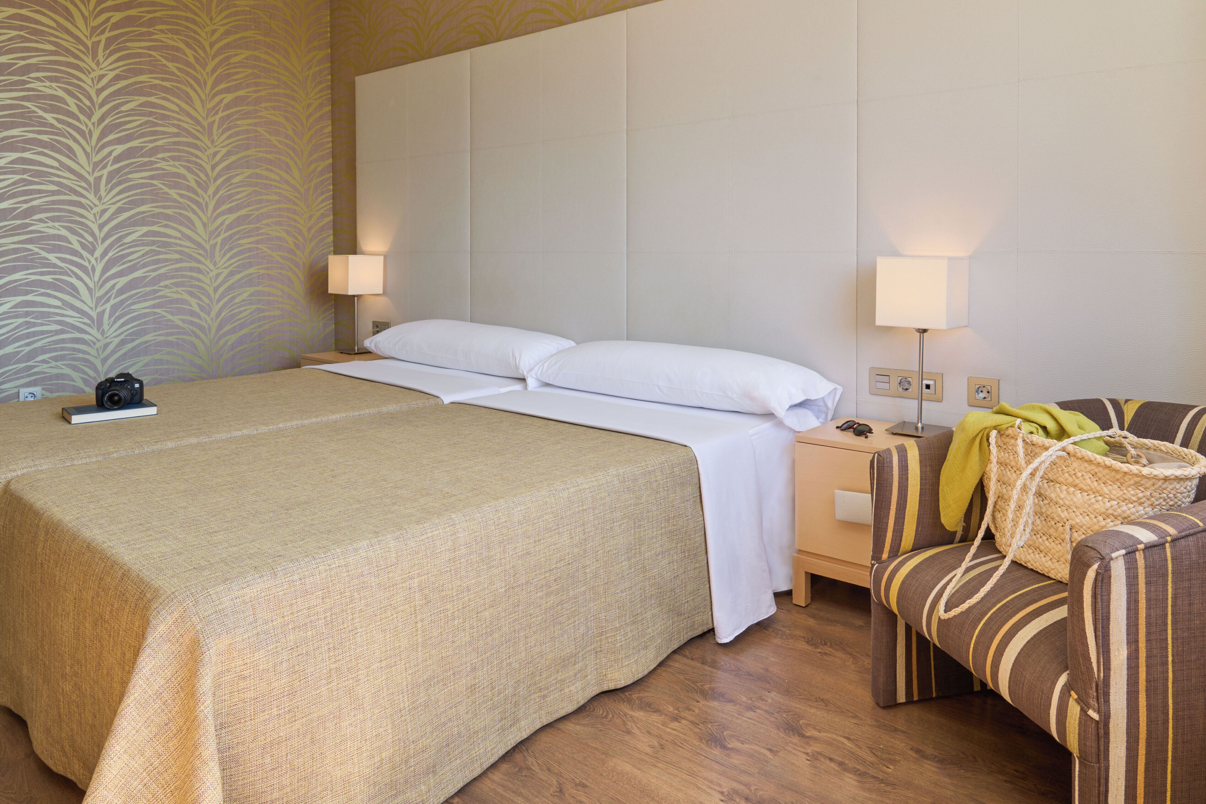 Une chambre d’hôtel avec un grand lit, deux tables de chevet, une chaise et un papier peint à motifs.