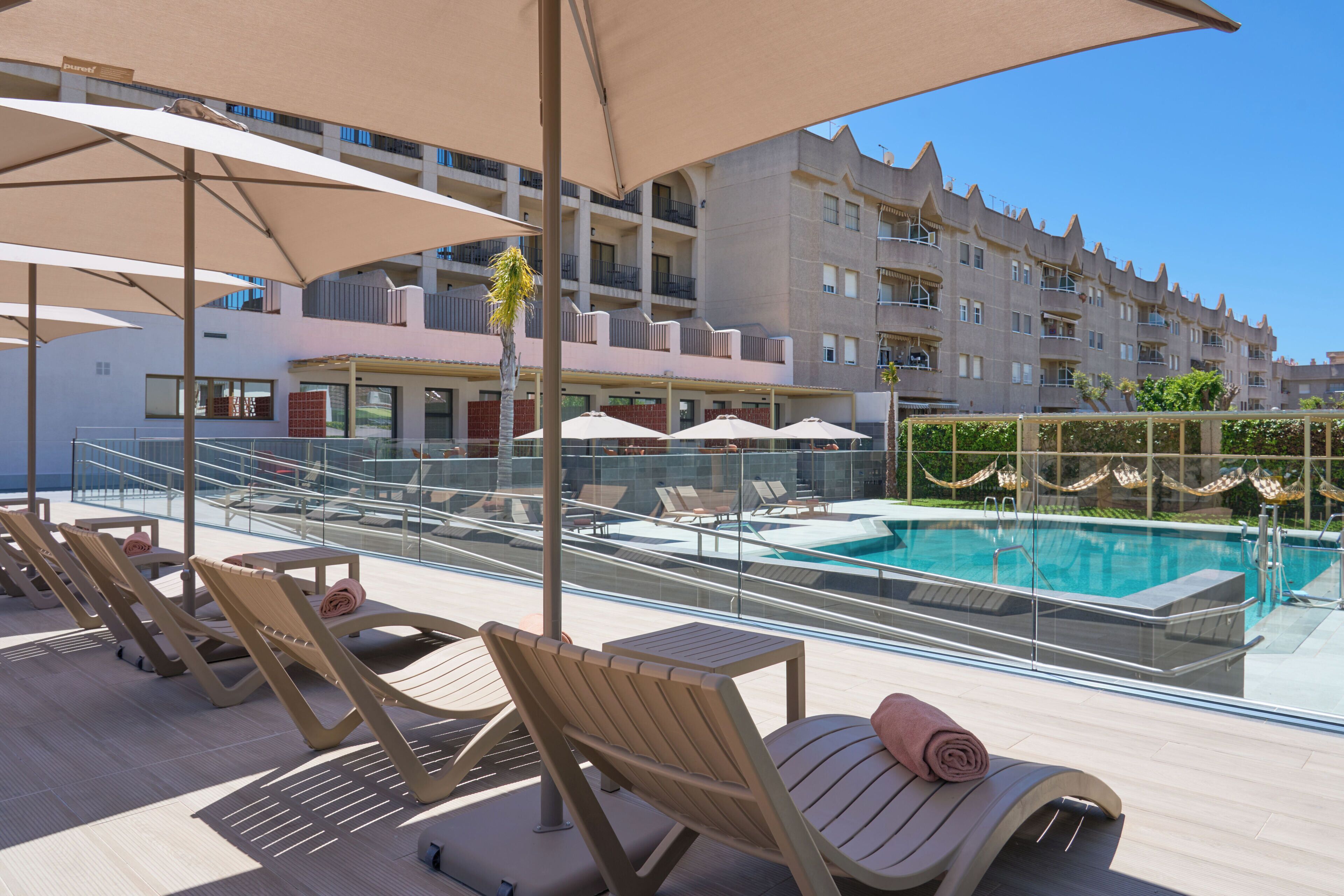 A rooftop pool area with lounge chairs and umbrellas, a clear view of the pool, and a modern building in the background.