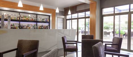 Uma área de bar moderna com diversos frascos de bebidas, assentos confortáveis e grandes janelas que oferecem vista para a área externa.