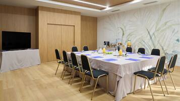 Un salón de conferencias con una larga mesa, sillas, un televisor y un mural en la pared.